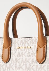 Sac à main Michael Kors beige et blanc avec poignées en cuir fauve et lettrage du logo doré sur tissu à motif.