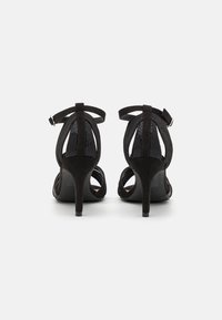 Juodi suflėniniai aukštakulniai šlepetės su tinklelio nugara, atvira pirštų dalimi ir kulkšnies dirželiu. Atskleidžia elegantišką siluetą ir turi 5 cm aukščio kulną.