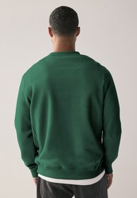 Zeleni dukserica s rebrastim izrezom i manžetama, glatke teksture, opuštenog kroja, prikazana sa stražnje strane.