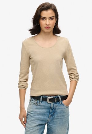 Beige lange mouwtop met een ronde hals, gemaakt van een zacht materiaal. G gedragen met hoge taille blauwe jeans en een zwarte riem met een zilveren gesp.