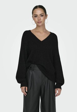 Pull noir en V avec une texture côtelée et de longues manches larges ; porté sur un pantalon en simili cuir noir taille haute. Fini en tissu lisse.