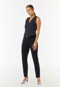 Marineblau gestreifter Anzugweste mit V-Ausschnitt und Knöpfen, kombiniert mit schwarzen Skinny-Jeans und silbernen High Heels. Glatter Stoff und taillierte Passform.