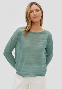 Lichtgroene doorzichtig lange mouwen top met horizontaal gestreepte textuur en een ronde halslijn, gedragen over off-white broek.