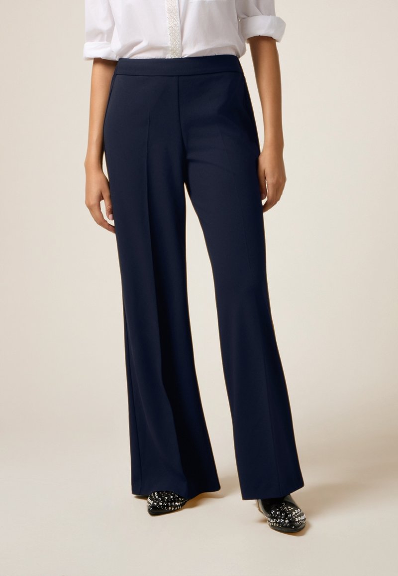 Navy wijde broek met een gladde textuur en een hoge taille, voorzien van voorplooien en gecombineerd met versierde zwarte instappers.