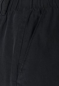 Los pantalones de tela negra cuentan con una textura suave, una cintura elástica y dos bolsillos laterales con detalles de costura.