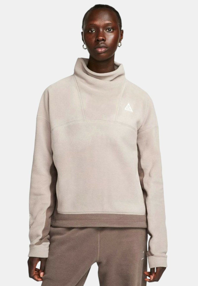 Felpa in pile beige chiaro con colletto alto, polsini a coste e un logo triangolare sul petto, abbinata a pantaloni coordinati.