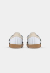 White sneakers with a gray and black design, featuring a gum sole and Velcro straps. Smooth material, rounded shape, and minimal stitching.