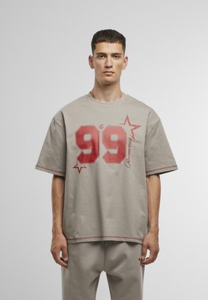 Oversized beige t-shirt made from cotton, featuring bold red "99" and star graphic, with contrasting stitching on sleeves and hem.