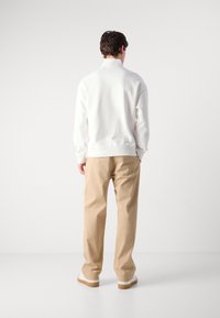 Felpa bianca con colletto alto, abbinata a pantaloni beige. Texture liscia, vestibilità rilassata. Design semplice, accenti minimi e calzature leggere.