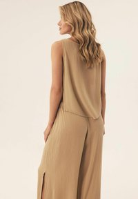 Beżowy top bez rękawów o luźnym kroju i plisowanej fakturze, zestawiony z szerokimi spodniami o luźnym kroju z bocznymi rozcięciami.