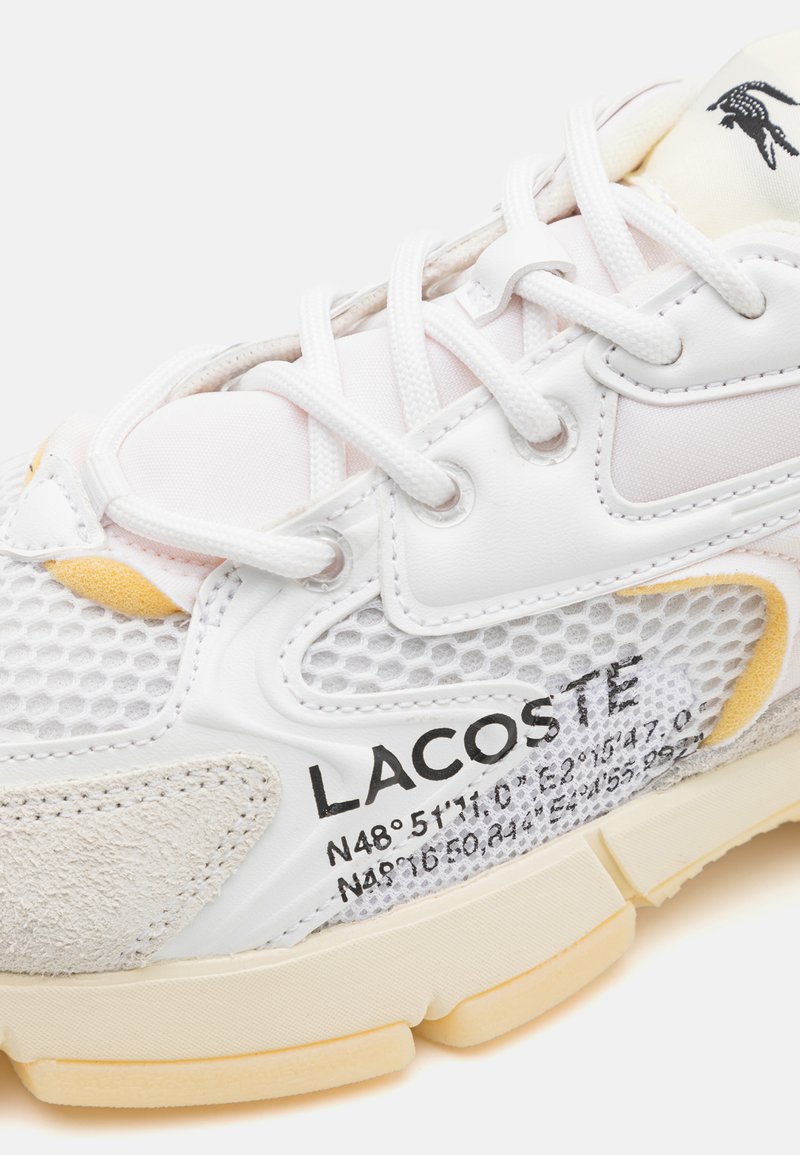 Zapatilla blanca que presenta materiales de malla y ante, cierre con cordones, marca prominente y coordenadas geográficas impresas en el lateral.