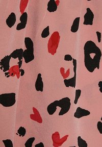 Tissu rose à texture lisse présentant un mélange de motifs abstraits de léopard en noir et rouge, parsemé de formes de cœurs.