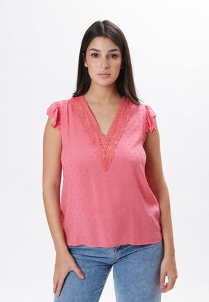 Blusa senza maniche rosa con scollatura a V e bordo in pizzo, caratterizzata da punti testurizzati e spalle arricciate. Abbinata a jeans in denim blu.