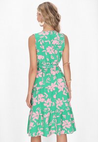 Rochie verde fără mâneci, cu un model floral roz, talie strânsă și tiv stratificat. Confecționată dintr-un material ușor, oferă o potrivire lejeră.