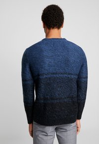 Pull en maille avec un dégradé de bleu foncé à noir, présentant un col arrondi et des poignets côtelés, avec une finition en tissu texturé.