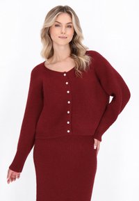 Burgundy stickad cardigan med rundad halsringning, långa ärmar och sex pärlknappar fram. Mjuk textur och kort design.