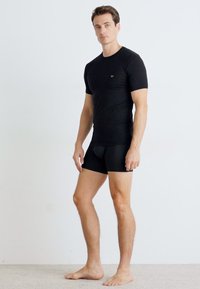 Tricou negru ajustat și pantaloni scurți dintr-un material neted. Tricoul are un logo minimalist și mâneci scurte, având un design fără cusături.