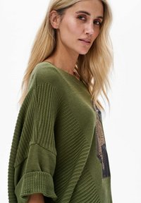 Sweter dziergany w oliwkowej zieleni z teksturalnymi wzorami, szerokimi rękawami i okrągłym dekoltem, z nadrukowanym wzorem z przodu.