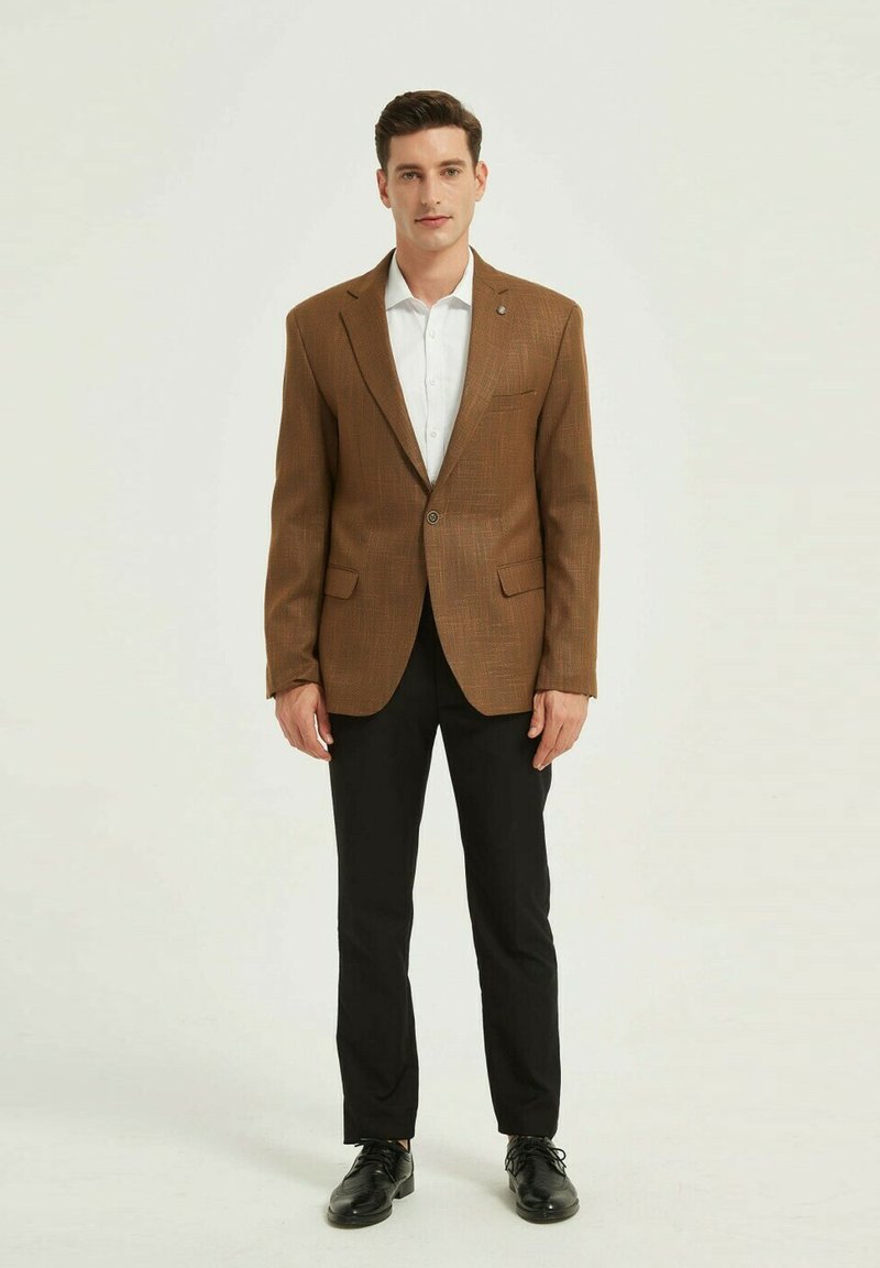 Blazer marron texturé avec revers crantés, fermeture à un bouton, et deux poches avant, assorti à une chemise blanche et un pantalon noir.