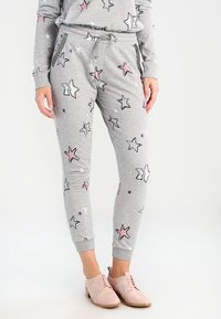 Person trägt graue Jogginghosen mit pinken und schwarzen Sternmustern sowie einen passenden Pullover, kombiniert mit hellrosa Oxford-Schuhen.