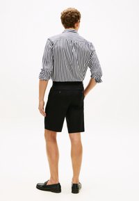 Μαύροι σορτς με στενή εφαρμογή συνδυασμένα με ένα λευκό πουκάμισο με μαύρες ρίγες. Σημαντικές λεπτομέρειες περιλαμβάνουν τα γυρισμένα μανίκια και το υφασμάτινο με υφή.