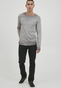 Langærmet grå T-shirt med en glat tekstur og rund hals, parret med sorte slim-fit jeans og sorte sneakers.