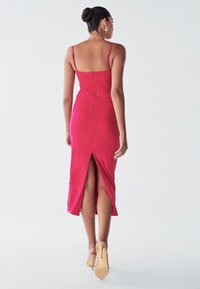 Fitted mid-length dress in vibrant pink, featuring a sleek silhouette, spaghetti straps, and a back slit for added movement.