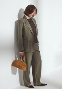 Oliwkowy, dopasowany garnitur z podwójnym zapięciem i szerokimi spodniami. Noszony z brązową koszulą, czarnymi balerinami i torebką z zamszu w kolorze jasnobrązowym.