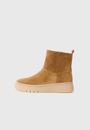 Beige Wildlederschuhe mit rundem Zehenbereich, strukturiertem Obermaterial und dicker beige Sohle. Mit einer Schlaufe an der Rückseite für einfaches An- und Ausziehen.