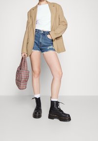 Blazer beige oversize, top corto blanco, pantalones cortos de mezclilla azul rasgados, botas negras con cordones y suelas gruesas, bolso a cuadros.