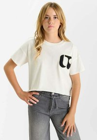 T-shirt blanc cropped en coton avec un détail de poche brodé noir. Assorti à un pantalon taille haute gris. Texture lisse.