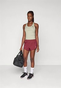 Sportinė tank top tipo palaidinė šviesiai žalia spalva, bordo spalvos šortai, juodi sportbačiai, balti kojinaitės ir juoda duffel tipo rankinė. Drabužiuose ir rankinėje matomas Puma logotipas.