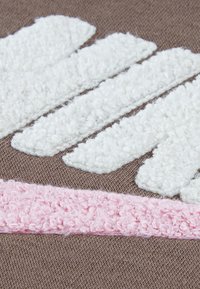 Textília s hnedým základom a bielymi, textúrovanými pruhmi a ružovým terry povrchom. Dizajn obsahuje nadýchané, vystúpené povrchy.