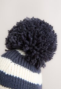 Gestrickte Wintermütze mit marineblauen und cremefarbenen Streifen, gekrönt von einer großen, flauschigen Bommel aus strukturiertem Garn.