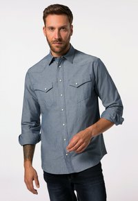 Modrá chambray košile s dlouhými rukávy, zapínáním na knoflíky vpředu, dvěma náprsními kapsami a ohrnutými manžetami. Má jemnou texturu a patentní knoflíky.