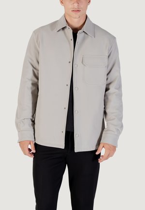 Chaqueta gris claro hecha de un material suave, con cierre de botón, collar puntiagudo y un bolsillo delantero con una solapa rectangular.