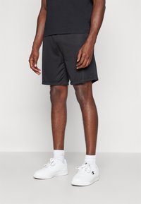 Zwarte sportshorts van lichtgewicht materiaal, met een elastische tailleband en zijzakken, gecombineerd met witte sneakers en sokken.