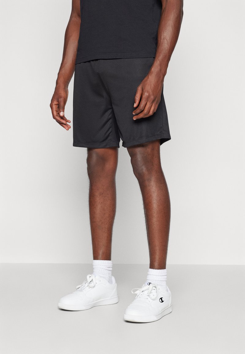 Zwarte sportshorts van lichtgewicht materiaal, met een elastische tailleband en zijzakken, gecombineerd met witte sneakers en sokken.