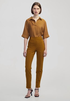 Brown collared shirt with short sleeves paired with high-waisted mustard trousers and black heeled sandals. Smooth fabric, fitted design.