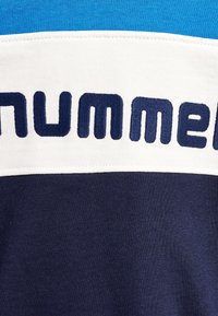 Primo piano di un pannello di tessuto con strisce blu, bianche e blu navy e lettere cucite in grassetto blu navy sulla parte bianca.