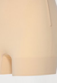 Pantalones cortos sin costuras en color beige, con una textura suave, diseño ajustado, longitud hasta mitad del muslo y una costura sutil a lo largo de la cinturilla y el dobladillo.