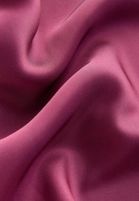 Gladek, neprozoren material v globoko rožnati barvi z mehkimi odsevi. Pada v nežnih valovih, kar prikazuje subtilno teksturo in enotno površino.