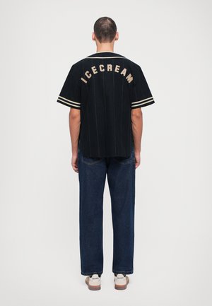 Zwarte jersey shirt met verticale strepen, korte mouwen en "ICECREAM" geborduurd in tan op de achterkant. Gepaard met blauwe denim broek en schoenen.