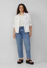 Witte denimjas met zilveren knopen over een gestippeld topje, gecombineerd met lichtblauwe rechte jeans en zwarte plateau-sandalen.