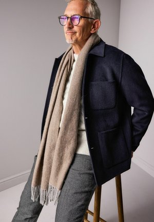 Navy wool overcoat with two chest pockets, beige herringbone scarf, cream ribbed sweater, and gray textured trousers. Clear, stylish design.