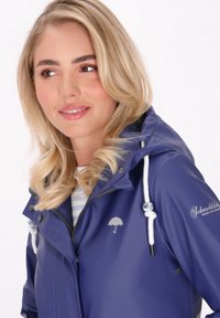 Lila vattentät jacka med huva, dragkedjestängning, dragsko och en liten paraplylogotyp. Har en slät textur och kontrasterande dragsko-accenter.