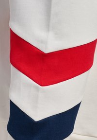 Hvidt stof med røde og navy blå chevronstriber, der viser tekstureret strikket materiale og overlappende farveblokke i en dragtærme.