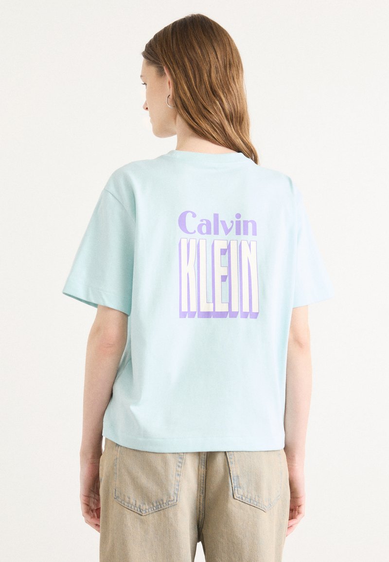Lichtblauw T-shirt met korte mouwen van katoen, uitgerust met "Calvin KLEIN" in vet paars en witte letters op de achterkant.