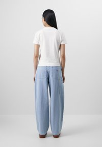 Hvit kortermet, tettsittende t-skjorte kombinert med lyseblå, vide jeans med to baklommer og et merke nær midjen.