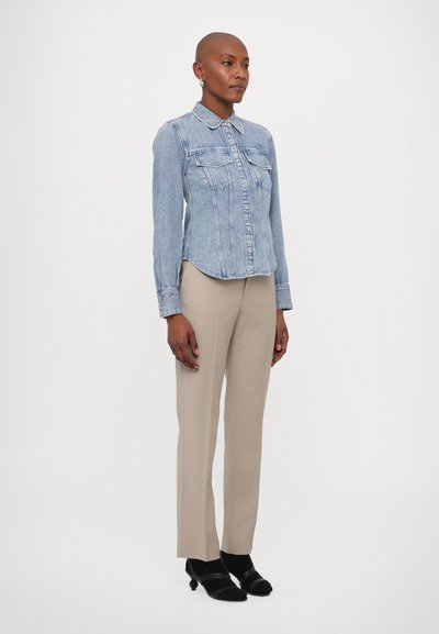 Lys blå denimskjorte med krage, to brystlommer og knappestolpen. Kombinert med lysebeige skreddersydde bukser og svarte hæler.